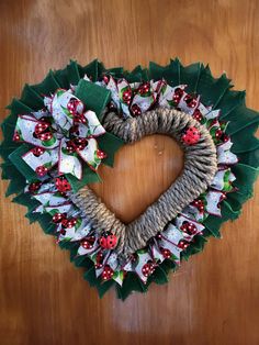 a heart shaped wreath with ladybugs and holly leaves on the front is hung on a wooden table