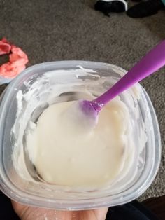 a hand holding a plastic container filled with ice cream and a purple toothbrush in it