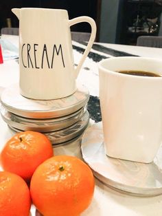 three oranges sitting on a table next to a cup and saucer with cream written on it