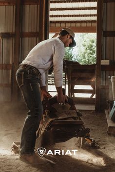 A man is getting his horse saddle ready to ride. He's wearing a tan Ariat trucker hat, a white Ariat long sleeve t-shirt, dark wash Ariat jeans, and brown Ariat leather cowboy boots. The Lifestyle, Fall Style, Brand You