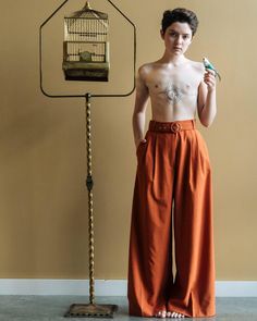 a young man standing in front of a bird cage holding an object with one hand