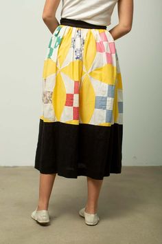 a woman standing in front of a white wall wearing a skirt with colorful squares on it