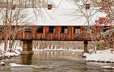 a covered bridge over a small stream in the woods with lots of snow on it