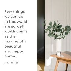 a vase filled with green leaves sitting on top of a wooden table next to a white wall