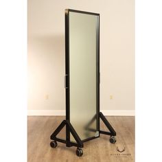 a tall mirror sitting on top of a wooden floor next to a black stand with wheels