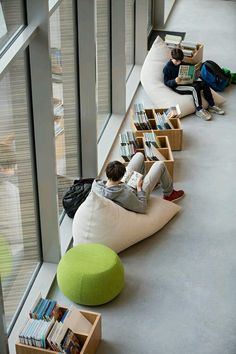 two people sitting on bean bag chairs reading books in a library with their backs turned to the floor