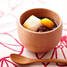 a wooden bowl filled with food next to a spoon on a red and white tablecloth