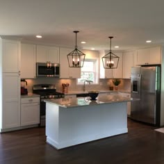 a large kitchen with an island in the middle and two pendant lights hanging from the ceiling