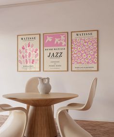 three posters hang on the wall above a round table with two chairs and a vase