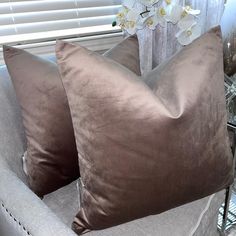 two brown pillows sitting on top of a chair next to a vase with white flowers