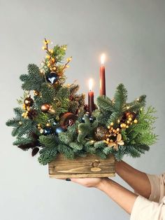 a person holding up a wooden box with candles in it and greenery on the inside