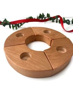 a circular wooden object with holes in the middle and holly on top, next to a red ribbon