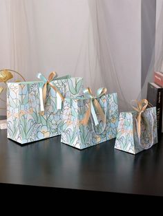 three small boxes with bows are sitting on a table next to books and a vase