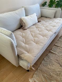 a white couch with pillows on it in front of a rug and potted plant