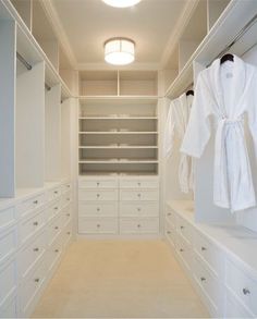 an empty walk - in closet with white cabinets and robe hanging on the door handles