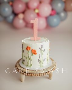 a white cake with flowers on it and a pink number one candle in the middle