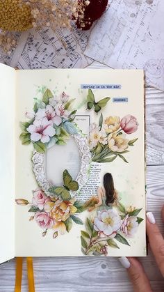 an open book with flowers on it and a person's hand holding the pages