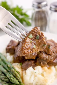 a fork with meat and asparagus on top of mashed potatoes