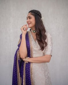 a woman wearing a purple and gold sari with her hand on her chin, posing for the camera