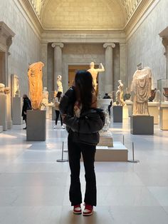 a woman is looking at some statues in a room with white marble walls and ceilings