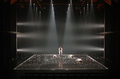 a man standing on top of a stage surrounded by spotlights in the middle of an auditorium