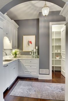 a white kitchen with gray walls and wood flooring is seen through an arch in the doorway