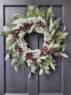 a wreath on the front door with berries and greenery hanging from it's sides