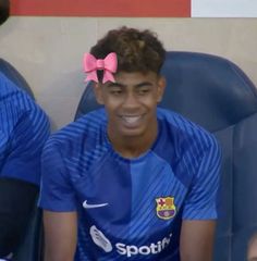 a young man with a pink bow on his head sitting in a blue soccer uniform