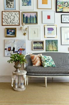 a living room filled with lots of framed pictures on the wall above a striped couch