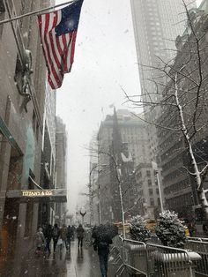 people walking down a street in the snow with an american flag hanging from a building