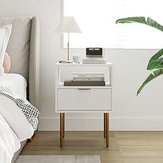 a bedroom with a bed, nightstand and plant on the side table in front of it