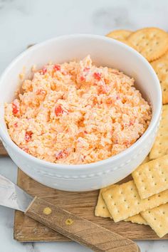 a white bowl filled with cheese and crackers on top of a wooden cutting board