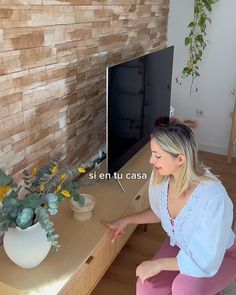 a woman sitting in front of a tv next to a table with flowers on it