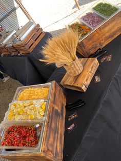 an assortment of food is displayed on a table with black cloths and wooden crates