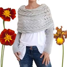 a woman standing next to two flowers with her hands on her hips and wearing a knitted shawl