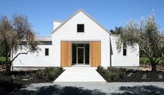 a white house with wooden doors and trees in the front yard on a sunny day