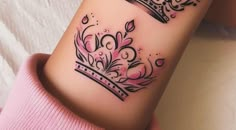 a woman's arm with a crown tattoo design on it, sitting on a bed