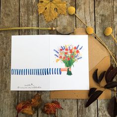 a card with flowers on it sitting next to some leaves and acorny plants