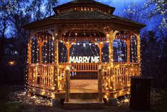 a gazebo covered in fairy lights with the words marry me written on it's side