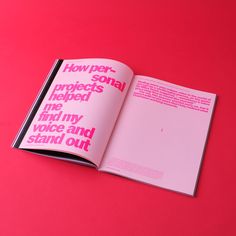 an open book with pink and black lettering on the cover, sitting on a red surface