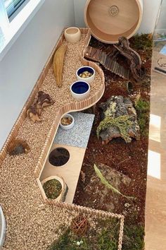 an animal habitat is shown with bowls and rocks in the ground, along with other animals