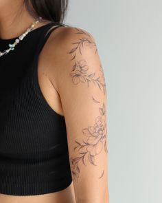 a woman wearing a black top with flowers on her arm and shoulder, looking at the camera