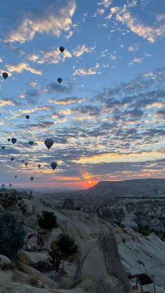 many hot air balloons are flying in the sky above some rocks and trees at sunset