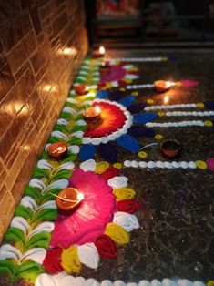 candles are lit on the ground in front of a brick wall and decorated with flowers