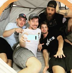 four men in a tent taking a selfie with a cell phone and pointing at the camera