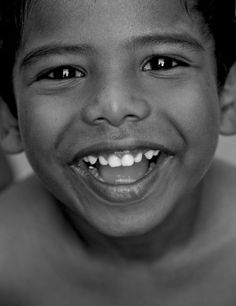 a black and white photo of a young boy with no shirt on smiling at the camera