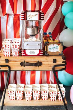 an old fashioned popcorn machine is set up for a movie themed birthday party with red and white striped balloons