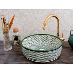 a green glass sink sitting on top of a wooden counter next to a vase and a faucet