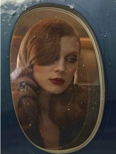 a woman with red hair is looking out an airplane window