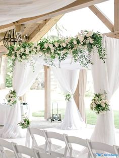 an outdoor ceremony with white flowers and greenery on the ceiling, draped drapes